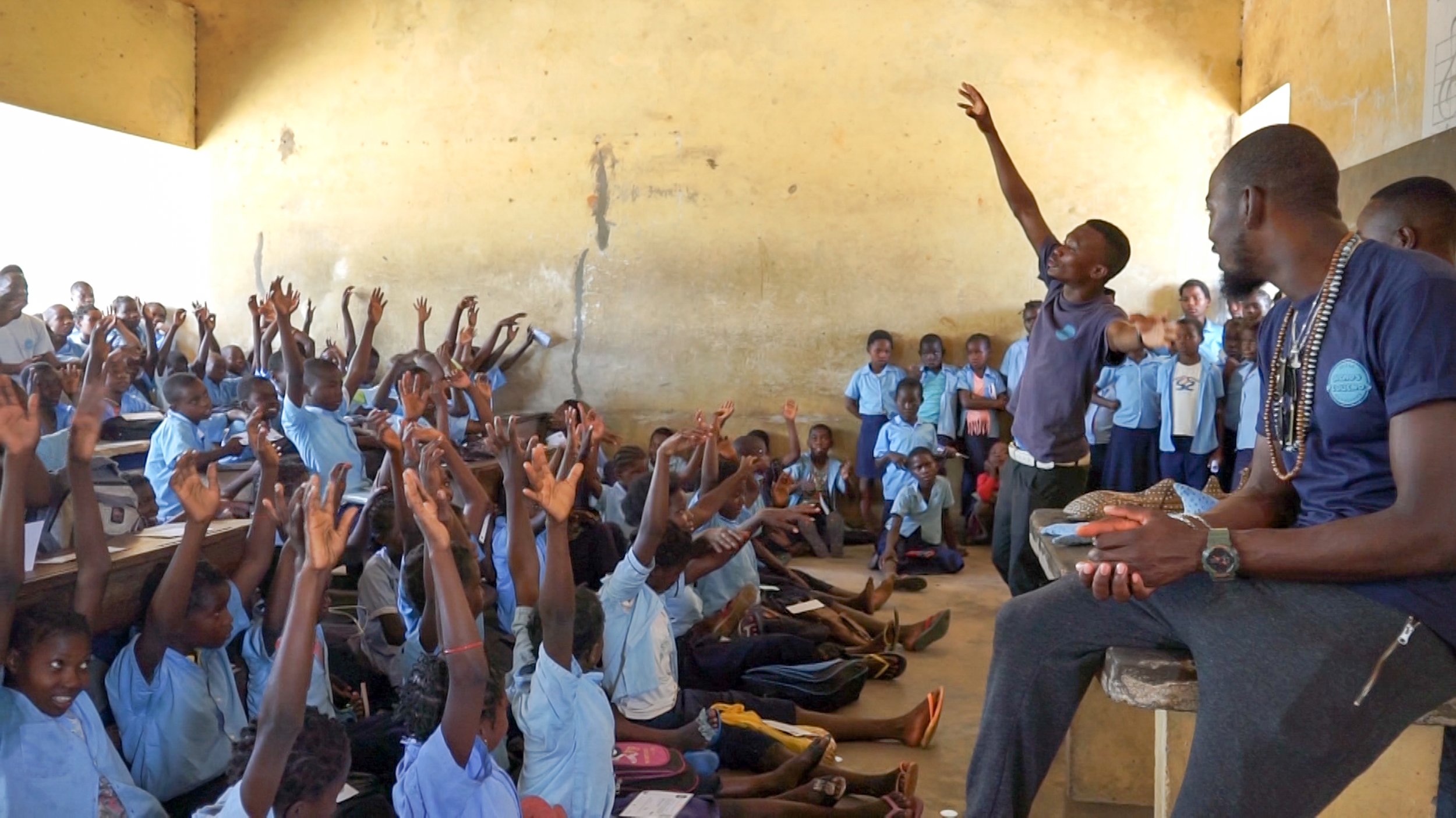 Children in a crowded classroom raise their hands during a marine conservation lesson