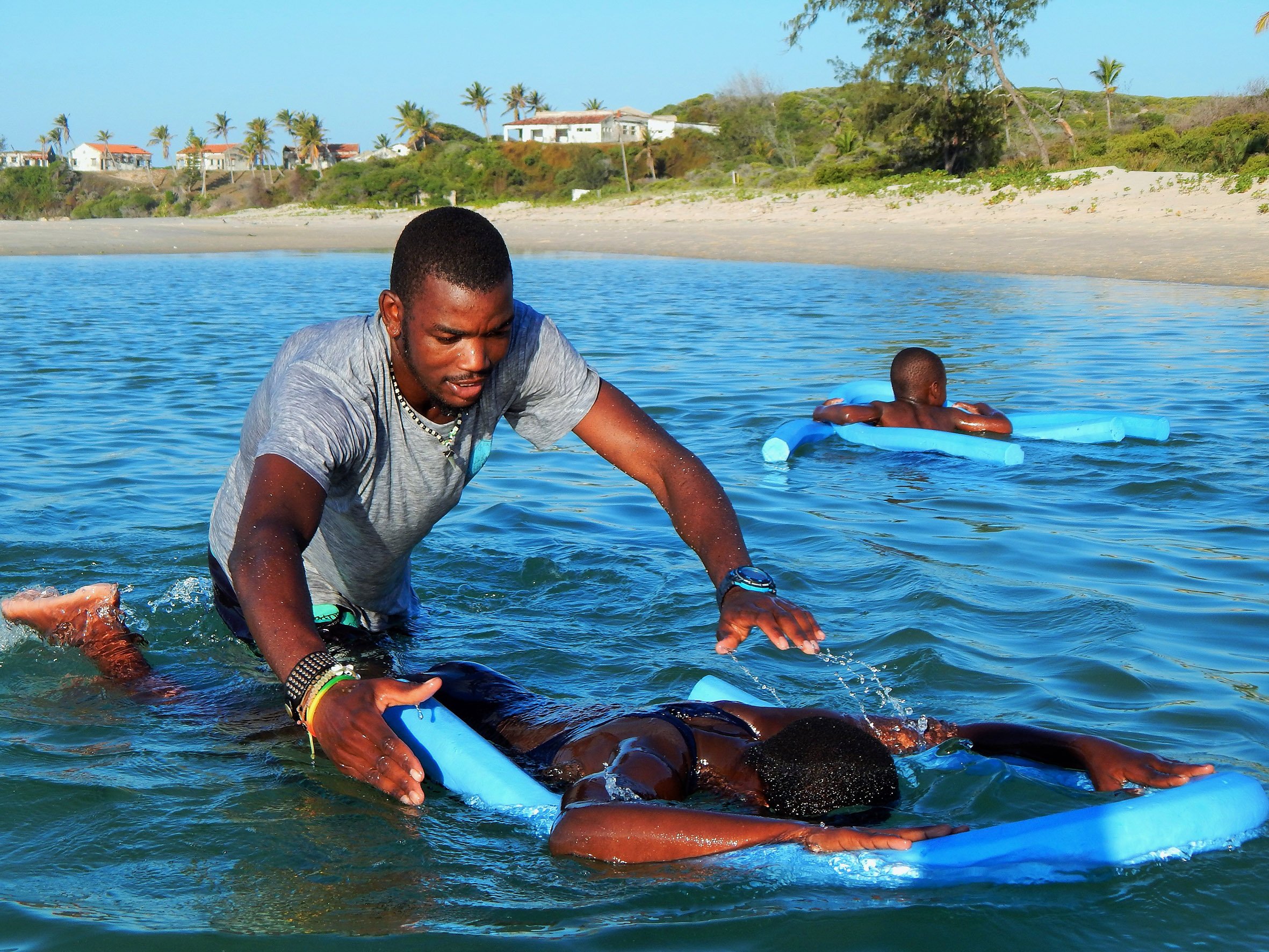 A swimming instructor supports a child floating on a pool noodle in the sea