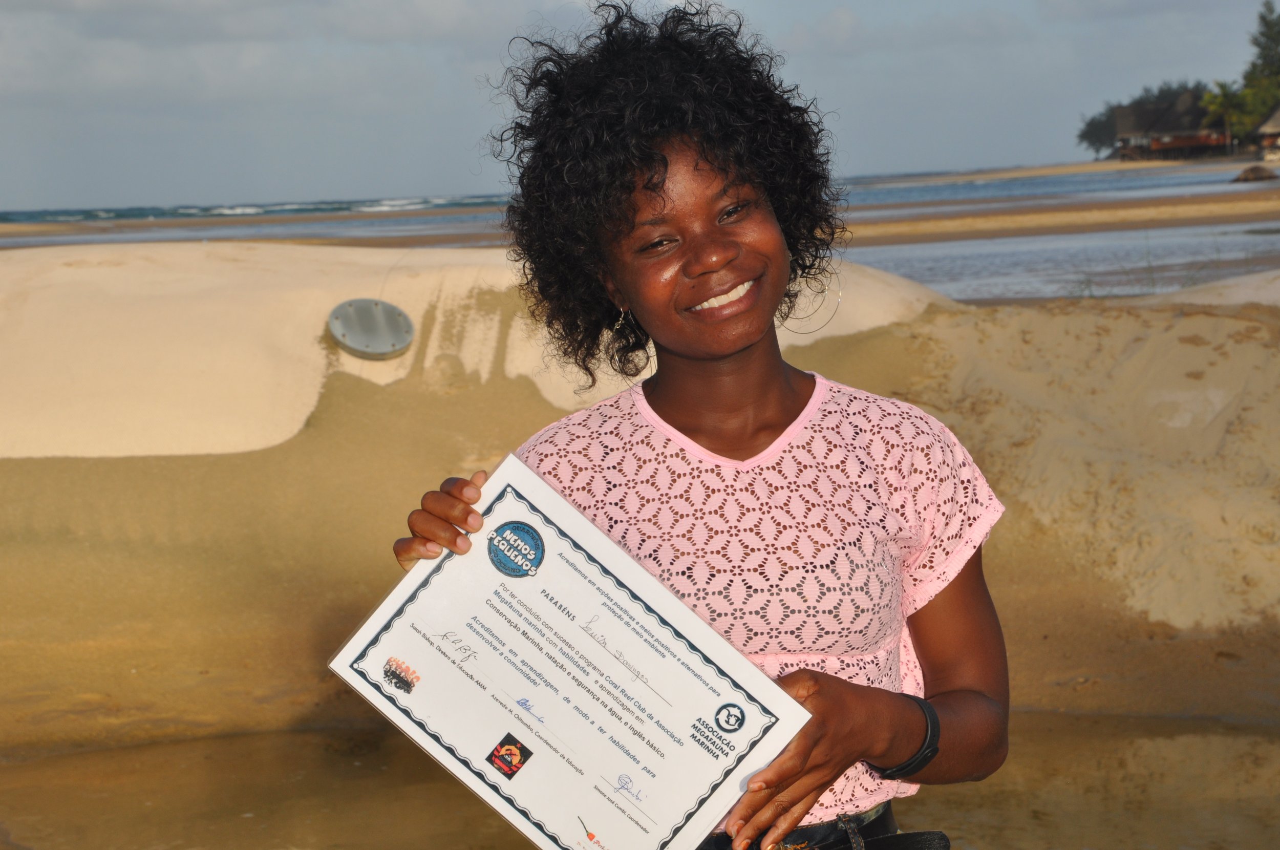 A young woman holds up her Ocean Guardians certificate on the beach