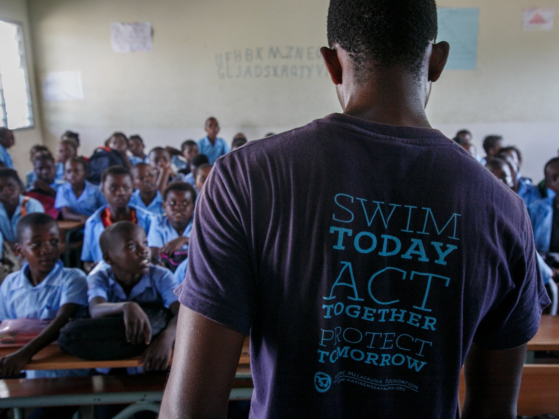 An instructor in a "Swim today, act together, protect tomorrow" T-shirt teaches a full classroom