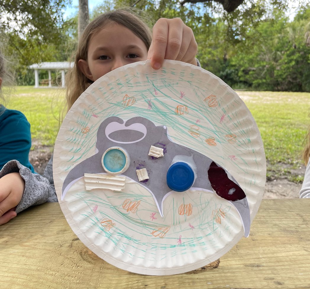 A student holds up a paper-plate manta ray made in class