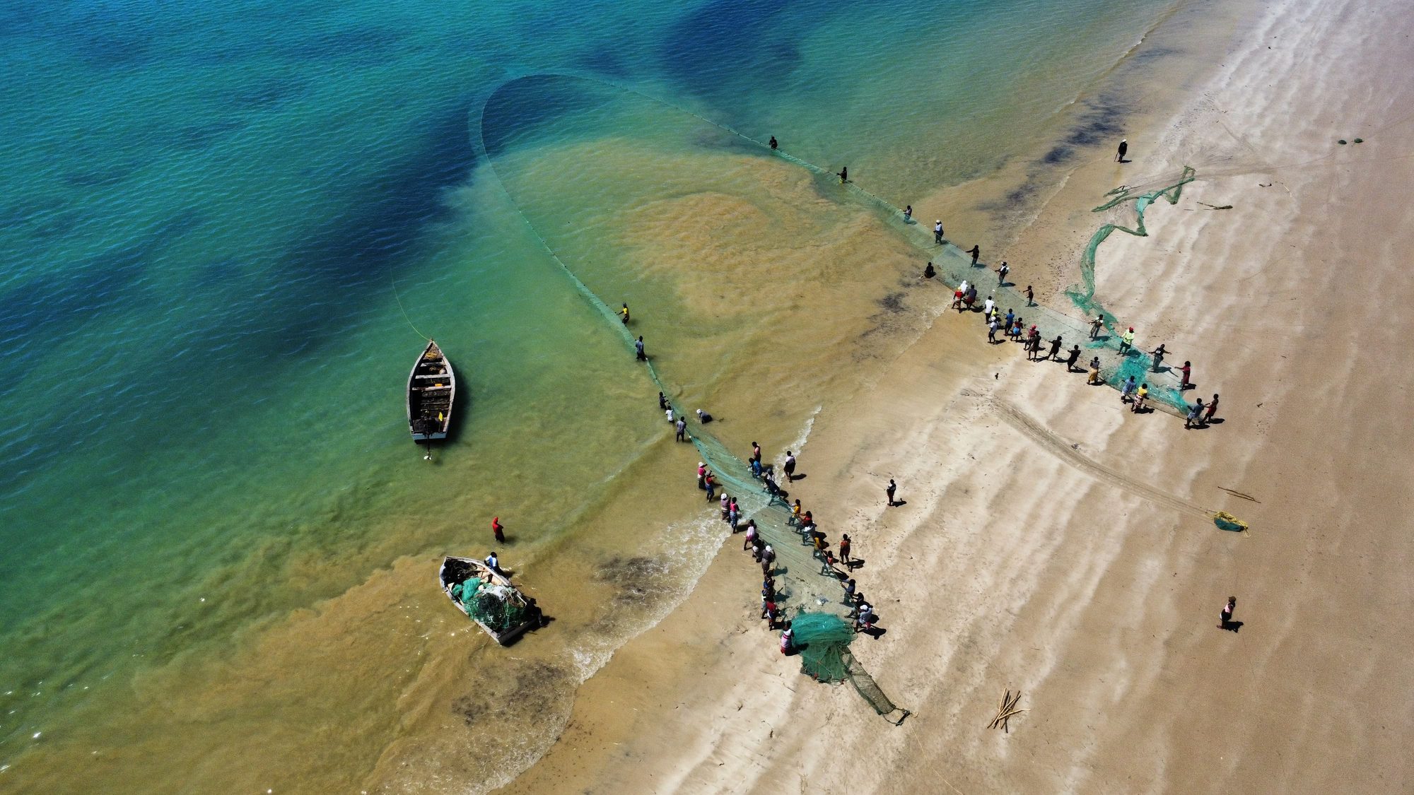 Seen from the air, fishers haul a drag net onto the beach through the shallows