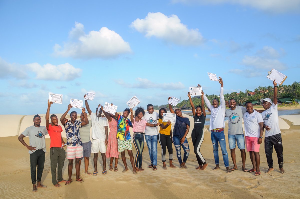Young people hold up their certificates on the beach